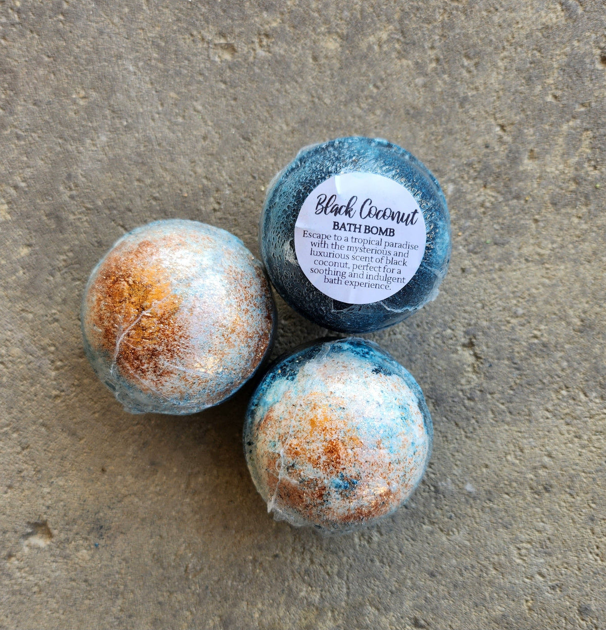 Three Herbal Island black coconut bath bombs in a whole pack, showing dark-colored spherical bath bombs with coconut scent.